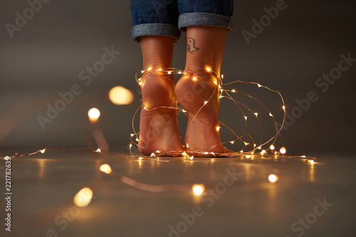 Composition of bright christmas lights decorating the feet of a young girl on a dark background