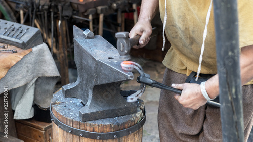 Blacksmith works a glowing metal on the anvil © kelifamily