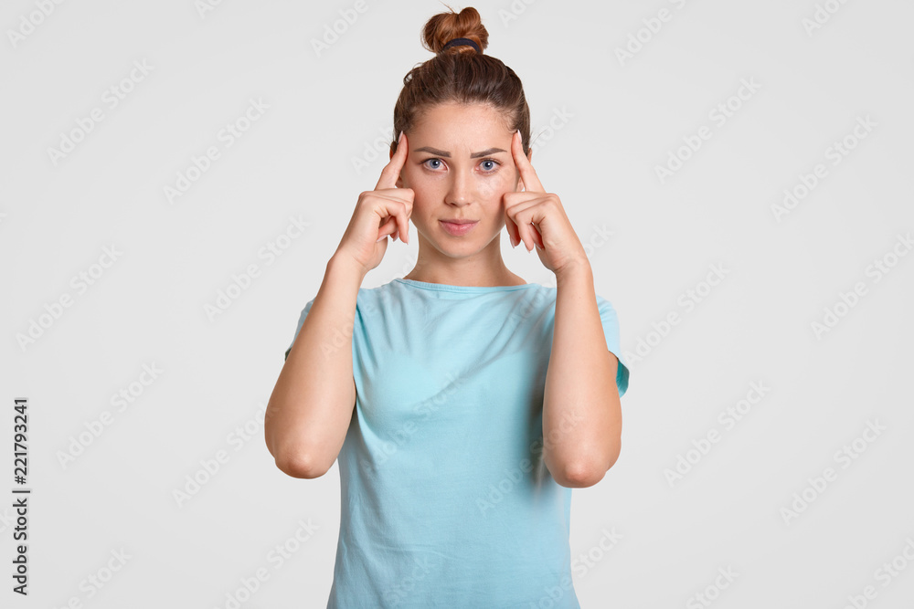 Photo of concentrated young female model tries to focuse on necessary information, keeps both index fingers on temples, has bad memory, dressed in casual clothes, isolated over white background Photo of concentrated young female model tries to focuse on necessary information, keeps both index fingers on temples, has bad memory, dressed in casual clothes, isolated over white background