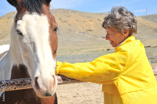 Mature female senior bonding with her horse on the ranch outdoors.