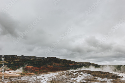 scenic view of landscape with volcanic vents under cloudy sky in Haukadalur valley in Iceland