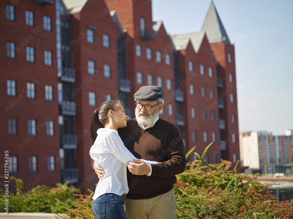 Fototapeta premium Help someone you love. Portrait of young smiling girl embracing grandfather against city park. community and family lifestyle concept