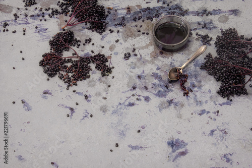 Frische reife violette schwarze Holunderbeeren gequetscht und gepresst und Holundersaft mit löffel auf rustikalem grauem blauem Hintergrund  photo