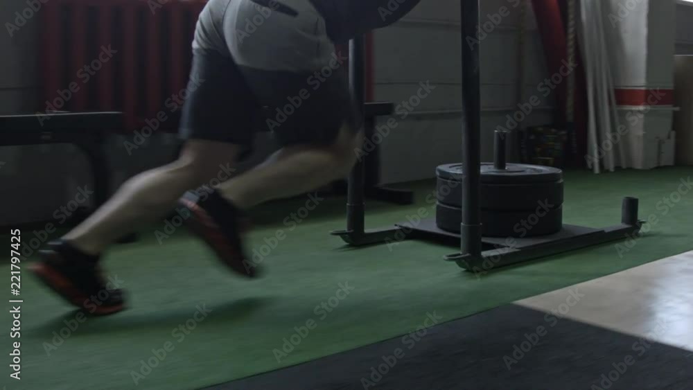 Sled push man pushing weights workout exercise at gym. Cross fit style