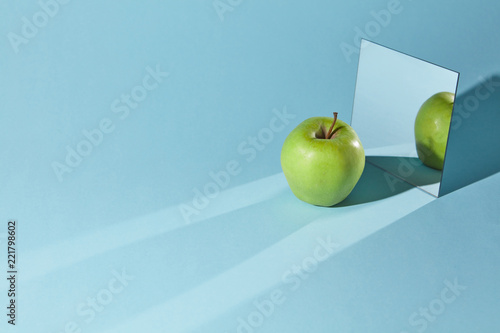 The apple is green, a square mirror on a blue background, a reflection of an apple and from shadows in a mirror.