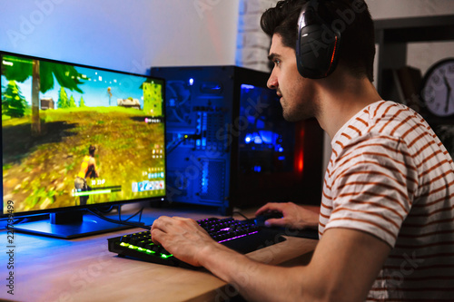 Foto Image of young man playing video games on computer, wearing headphones and using