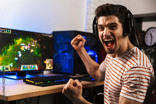 Fotografia Portrait of happy man playing video games on computer, wearing headphones and us