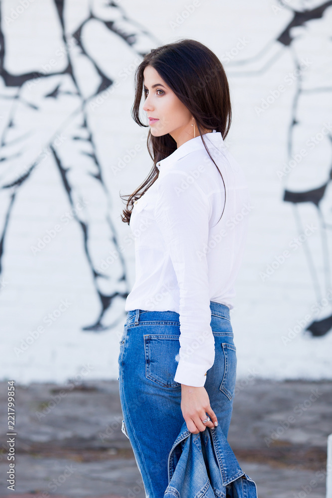 Hipster girl wearing blank white shirt, jeans and jeans jacket posing  against street wall. Minimalist urban clothing style, street fashion. Stock  Photo | Adobe Stock