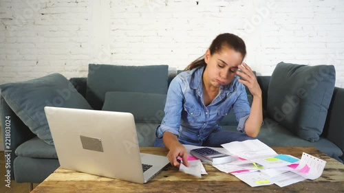 Portrait of worried young single mother feeling stressed while working through finances with laptop and calculator in living room in paying off debts and domestic bills and financial problems concept.