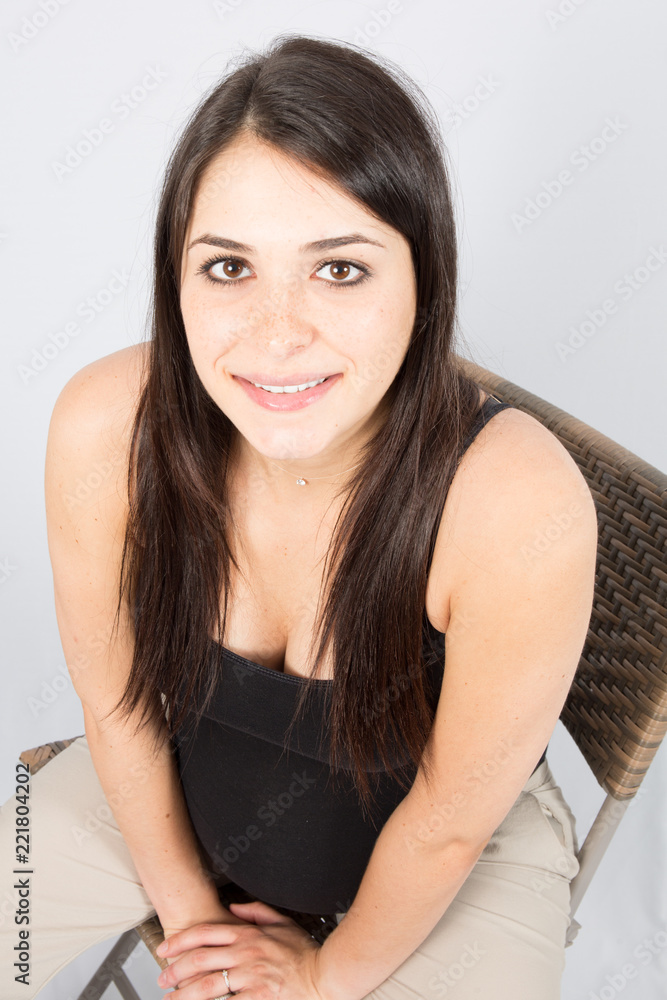 Studio shot of a beautiful young woman smiling, sitting on chair Studio shot of a beautiful young woman smiling, sitting on chair