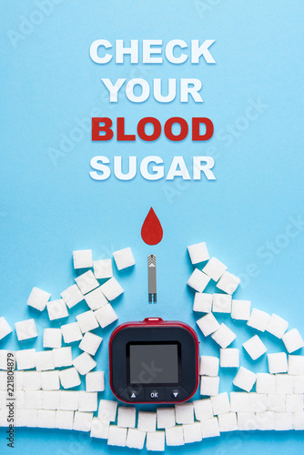 inscription check your blood sugar, red blood drop, wall made of sugar cubes ruined by Glucose meter on blue background