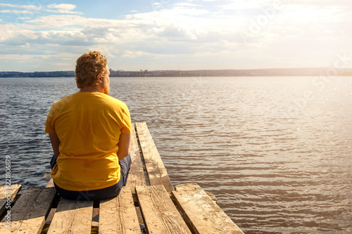 A man sits on a wooden pier and looks at the sea