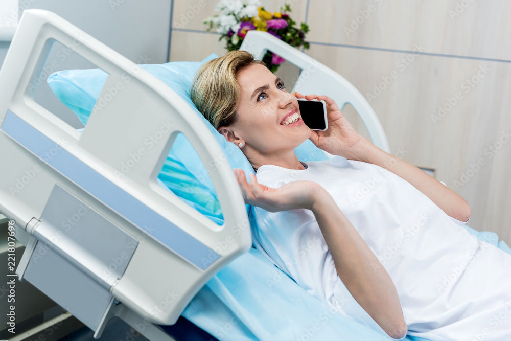 happy female patient laying on bed and talking on smartphone in hospital room happy female patient laying on bed and talking on smartphone in hospital room