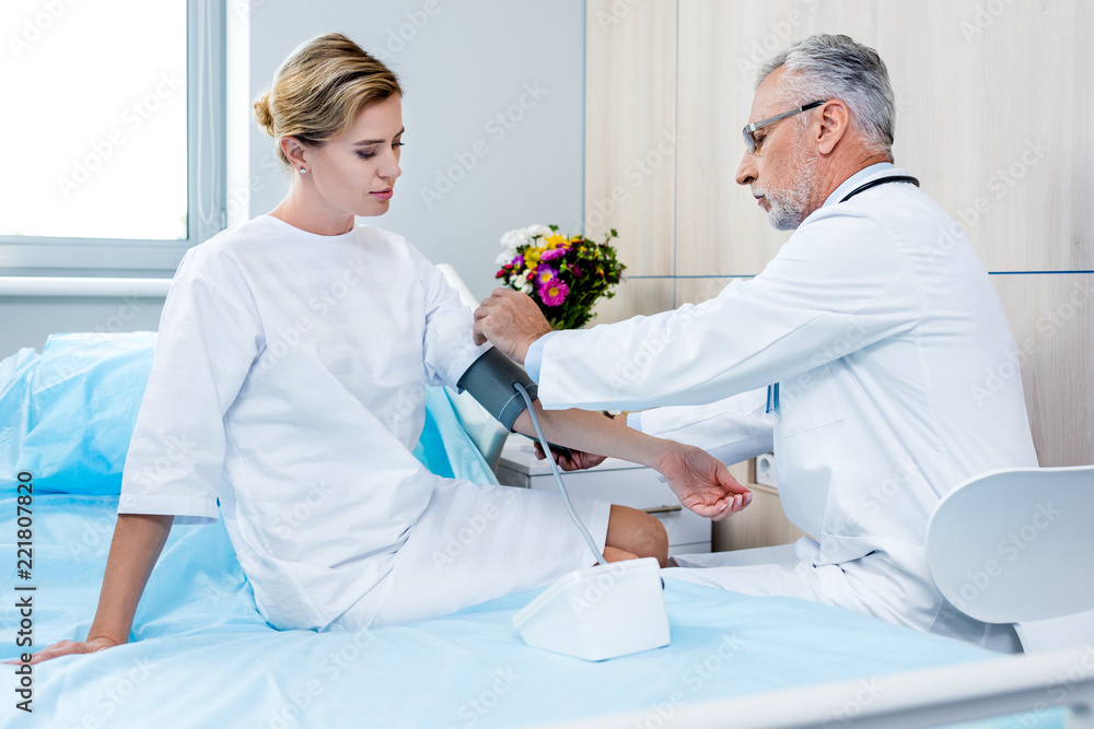 Fototapeta premium side view of middle aged male doctor putting on device for measuring pressure on female patient hand in hospital room