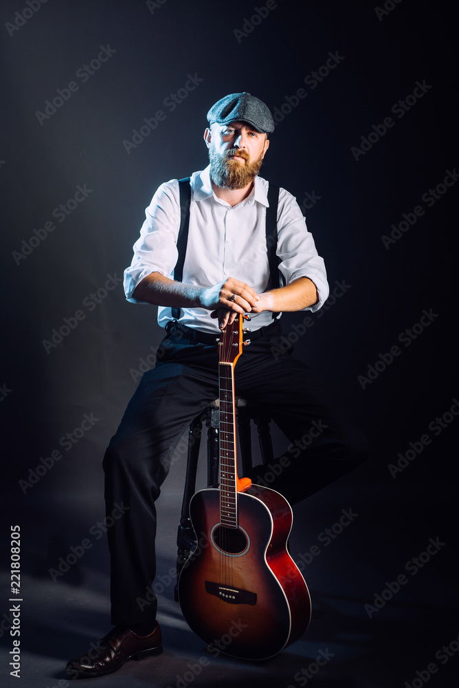 Fototapeta premium A bearded man in hat with guitar in studio