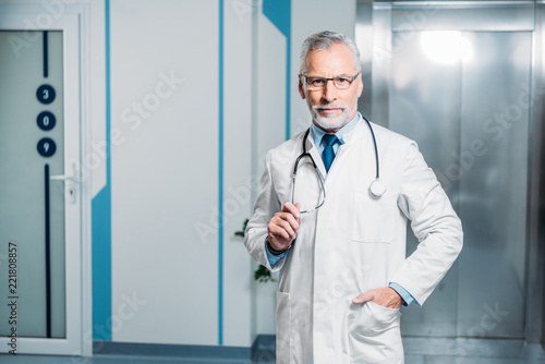 middle aged male doctor with stethoscope over neck looking at camera in hospital