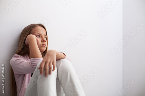 Pensive young teenager girl sitting by the wall on the floor photo