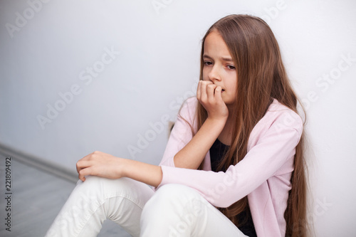 Worried young teenager girl sitting on the floor by the wall - medium portrait