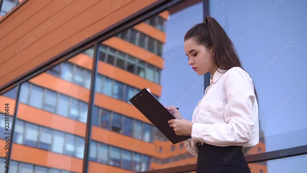 Business girl is making notes in working papers standing near business center. 4K Business girl is making notes in working papers standing near business center. 4K