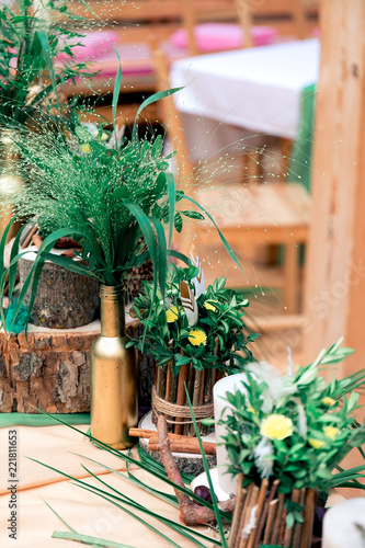 Rustic wedding decor in Eco style with different elements candles, bottles, sawed wood, branches, nuts, feathers and green leaves.