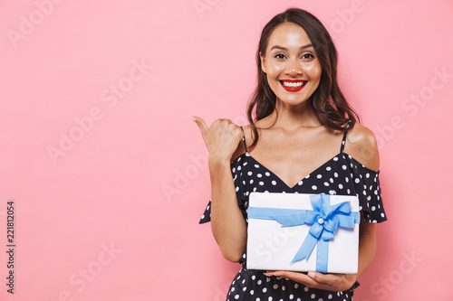 Happy woman isolated over pink background holding susprise gift box pointing. photo