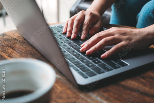 Closeup image of a woman's hands working and typing on laptop keyboard with coffee cup on wooden table