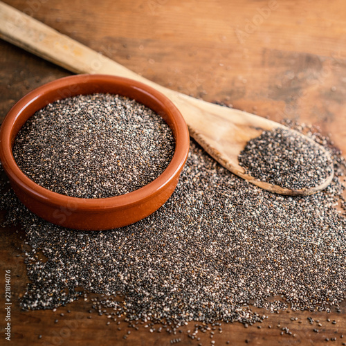 Chia seeds in a clay bowl and wooden spoon on wood background. Copy space..