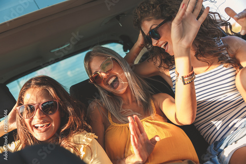 Three female friends enjoying traveling in the car. Sitting in rear seat and having fun on a road trip.