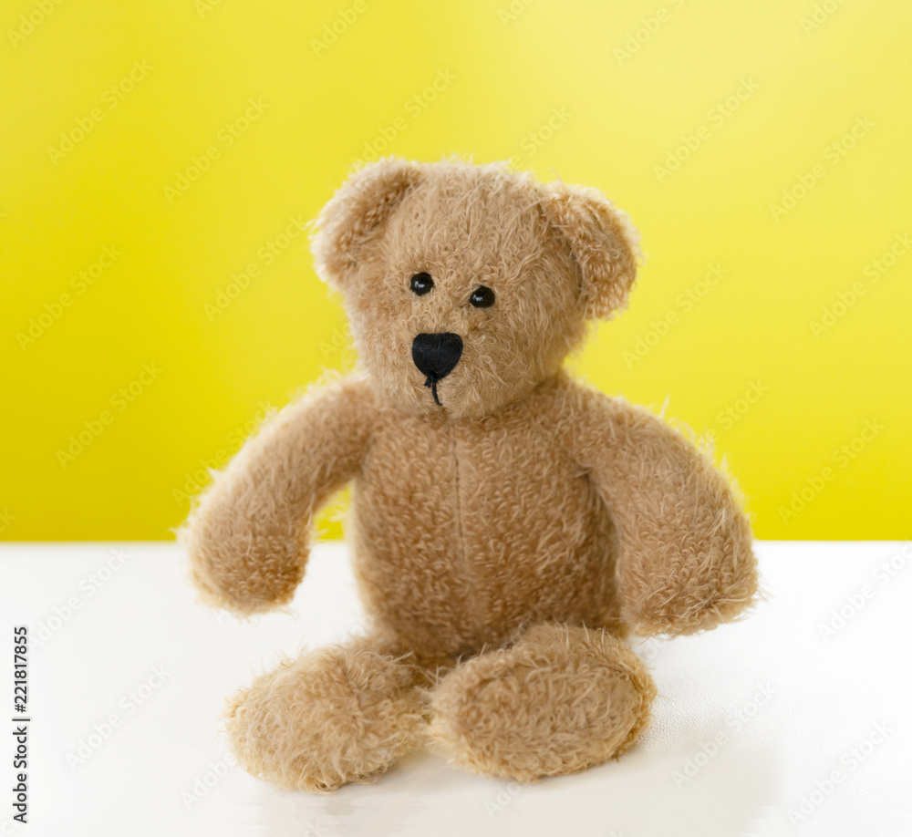 Portrait of teddy bear sitting alone on white table with yellow background, One brown bear toy with with copy space Portrait of teddy bear sitting alone on white table with yellow background, One brown bear toy with with copy space