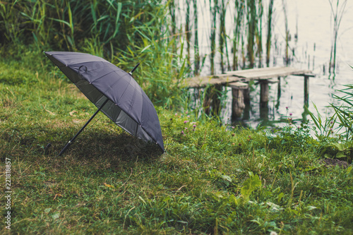 black open umbrella lay on grass wet autumn natural scenery environment near river waterfront with small wooden pier 