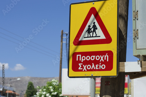 Triangle road sign "Caution children" sunlit and greek inscription (no trade mark) in Greece