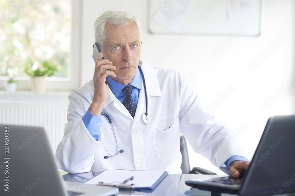 Male doctor making call. Shot of a doctor sitting at consulting room and talking with his patient on phone. Male doctor making call. Shot of a doctor sitting at consulting room and talking with his patient on phone.