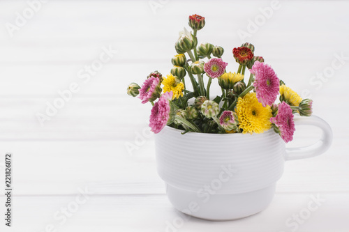 Fototapeta Naklejka Na Ścianę i Meble -  Unripe flowers in a white mug. White wooden table background.