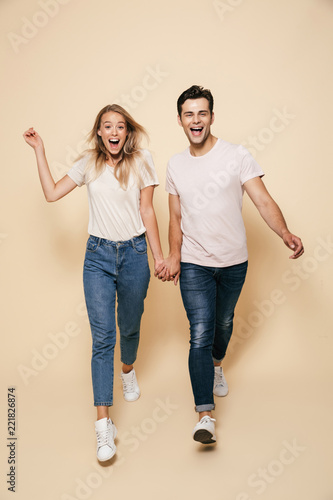 Young loving couple walking isolated over beige wall background.