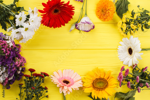 Bright colorful different flowers arranged around. Yellow wooden desk background.