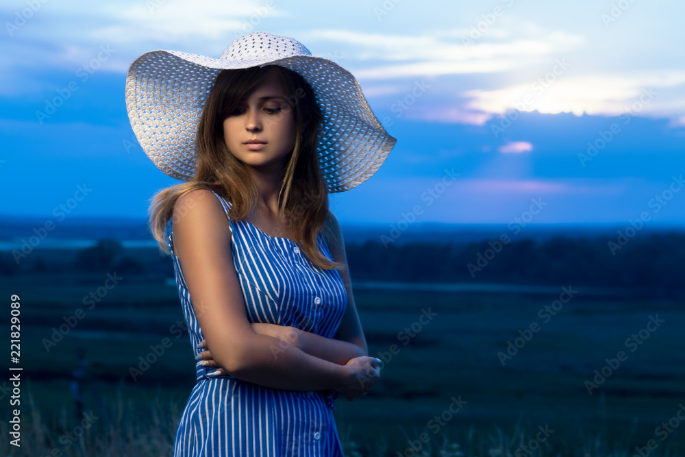 Fototapeta premium dramatic portrait of a beautiful girl in a hat in the field, a young woman is walking in the summer outdoors
