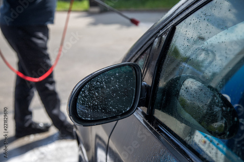 Mann nutz  Hochdruckstrahler mit Wasser um Reinigungsmittel  bei Autowäsche in Auto SB Waschbox abwaschen photo