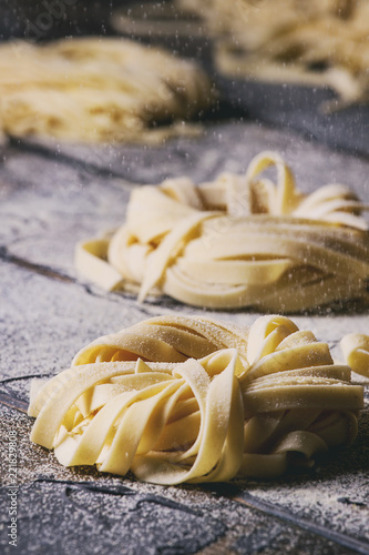 Variety of italian homemade raw uncooked pasta spaghetti and tagliatelle with sprinkling semolina flour over dark plank texture wooden table. Dark rustic style