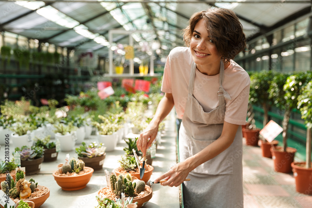 Cute woman gardener standing over flowers plants in greenhouse working Cute woman gardener standing over flowers plants in greenhouse working