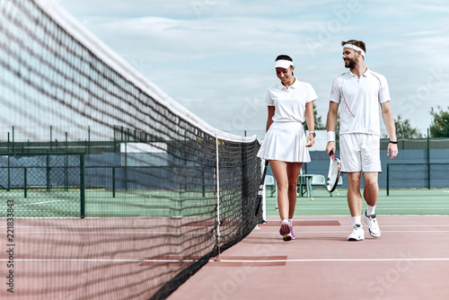 Enjoying spending time on the court. Beautiful young couple walking on the tennis court with smile.