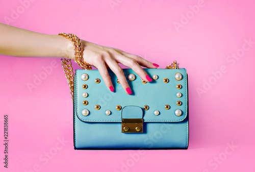 Sky blue handbag purse and beautiful woman hand with red manicure isolated on pink background. photo