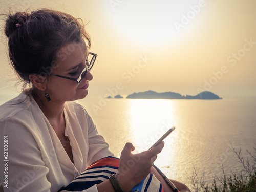 Young woman using smartphone at sunset in front of the sea on Ponza island coast © WineDonuts