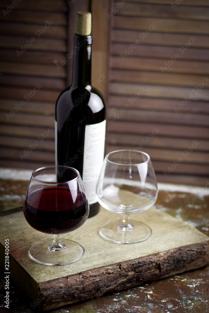 wine glass with expensive red wine,  blurred bottle of wine, wooden background