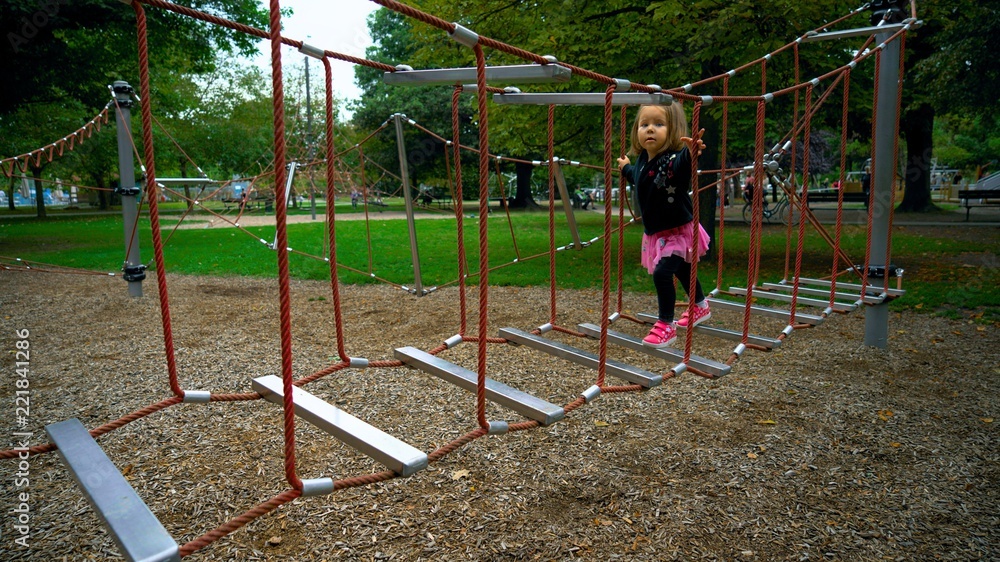 A little girl is playing on the playground and climbing the ropes. No image contains visible brand names or logos.