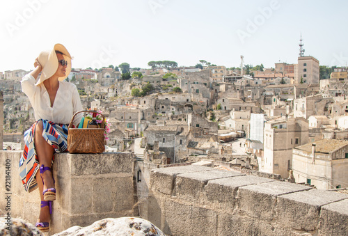 Young elegant woman tourist sitting in historical Matera town in Italy looking at city landscape photo