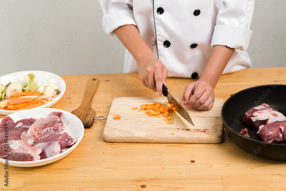 Asian preteen boy in chef uniform chopping carrot on table.