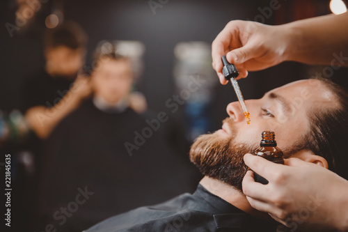 Barber applies beard oil with dropper for man in barbarshop. photo