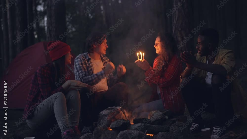 Creative people are congratulating their friend on birthday in forest, clapping hands and giving her cake while girl is blowing candles and smiling. Nature and celebration concept. Creative people are congratulating their friend on birthday in forest, clapping hands and giving her cake while girl is blowing candles and smiling. Nature and celebration concept.