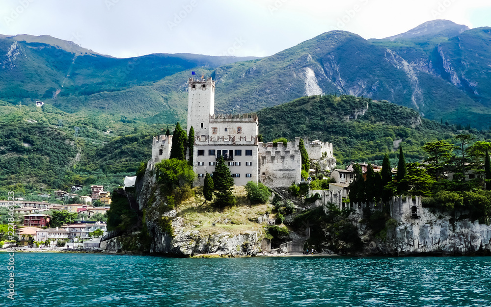 Fairytale landscape view of Malcesine Castle, Italy, from Lake Garda, with part of the Monte Baldo mountain group in background. Distant views of the lakeside town. Trentino.