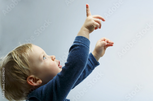Beautiful blonde toddler looking up. Boy showing, kid holding his hand up. Copy space